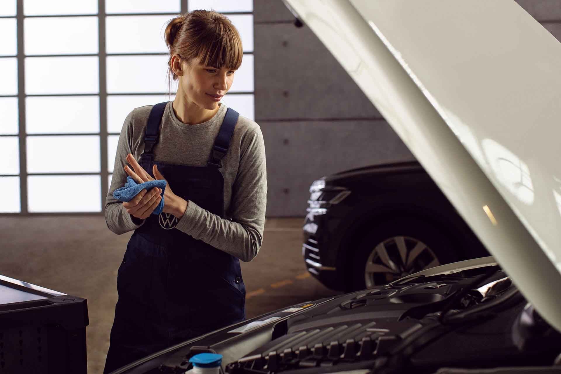 Un meccanico controlla il motore di un'auto Volkswagen con il cofano aperto.