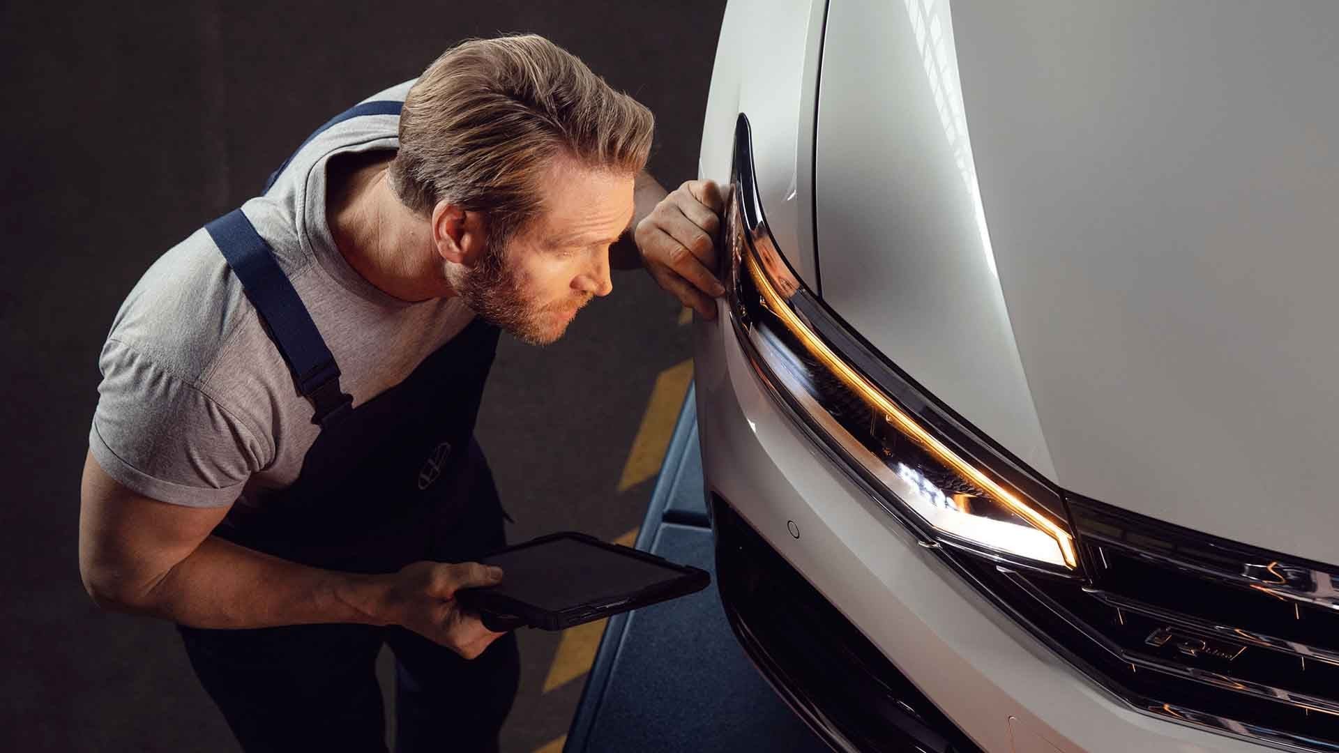 Un meccanico Volkswagen controlla le luci del faro anteriore sinistro di una vettura, con l'aiuto del suo tablet."